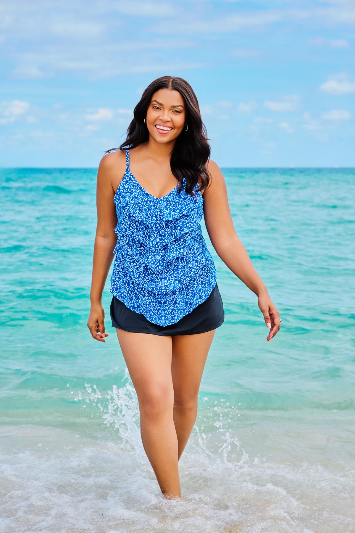Woman on beach wearing a blue scroll printed tankini top with ruffles