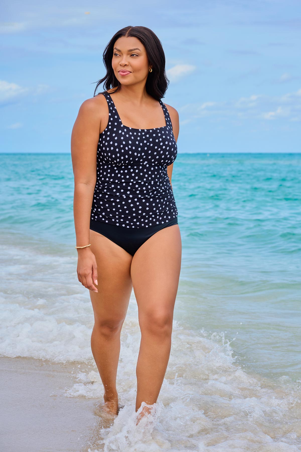 Woman on beach wearing a one-piece swimsuit with a black and white polka dot print