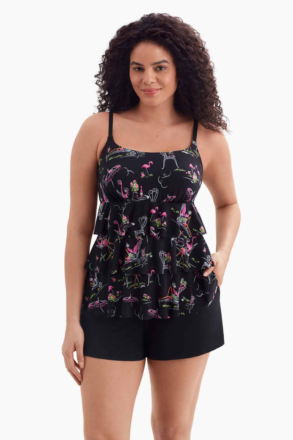 Woman wearing a one-piece tiered swimsuit with a flamingo print with her hand in pocket