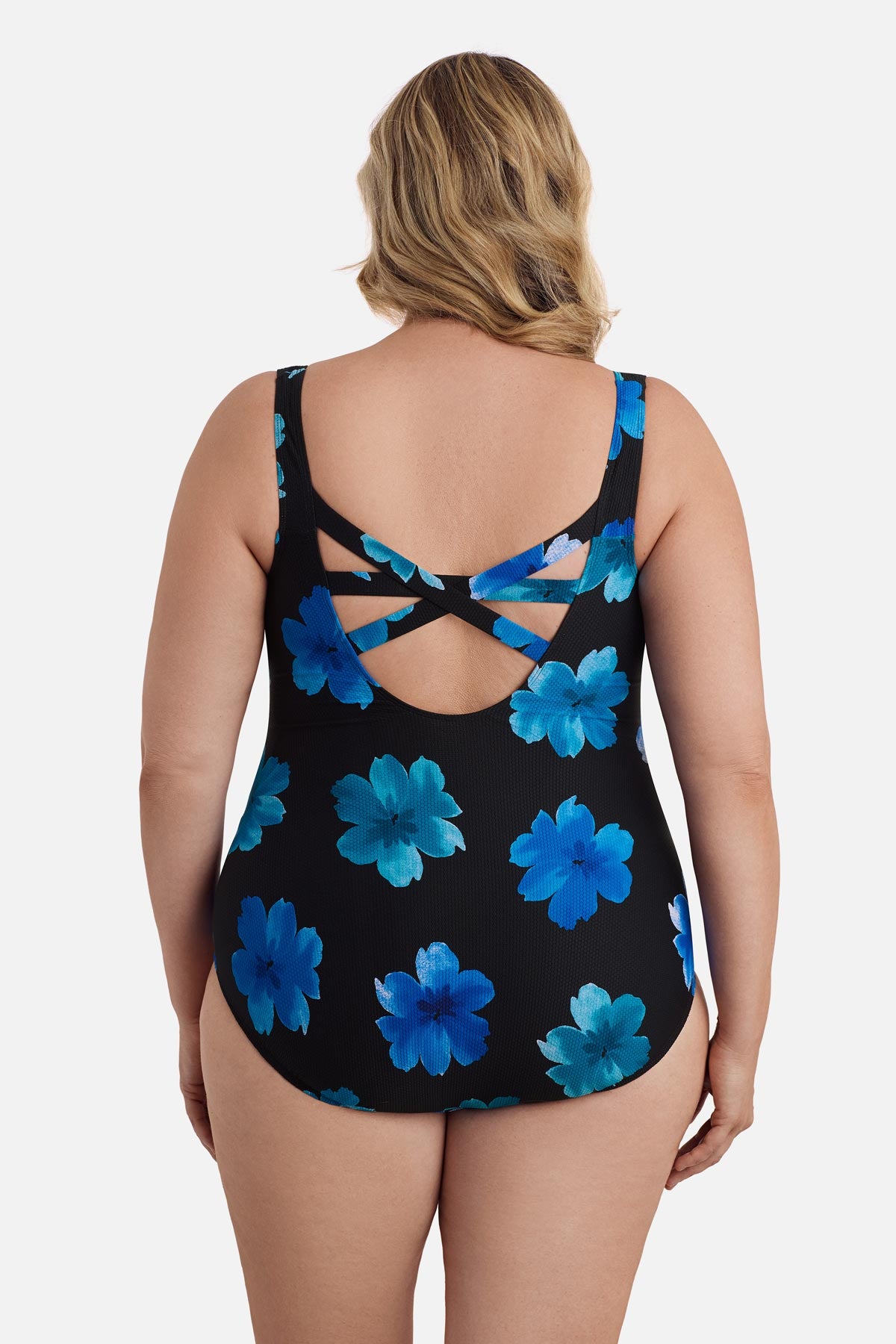 Woman faced away wearing a large blue flower printed one-piece swimsuit with an X back