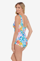 Woman faced left wearing a multicolored tropical print front ruffle one-piece swimsuit
