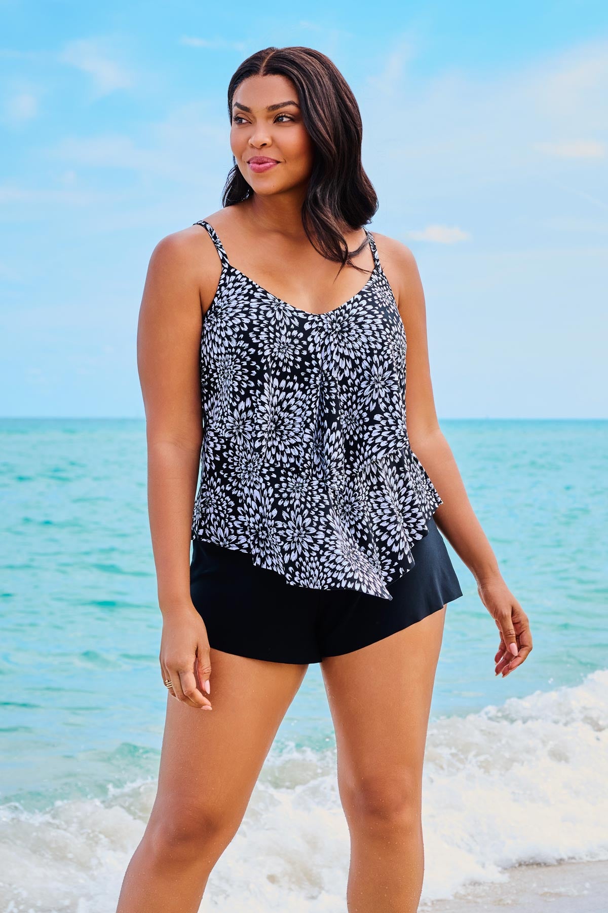 Woman on beach wearing a black and white floral printed tankini top with ruffles
