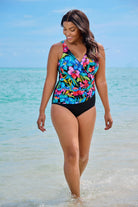 Woman on beach wearing a one-piece swimsuit with a multicolored floral pattern