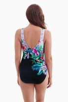 Woman turned away wearing half white half black one-piece swimsuit with a floral print running through the middle