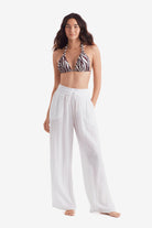 Woman wearing a zebra print bikini top with white beach pants