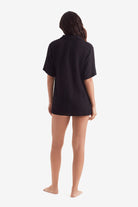 Woman faced away wearing a black short sleeve button up shirt