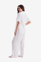 Woman turned left wearing a white short sleeve button up and white beach pants