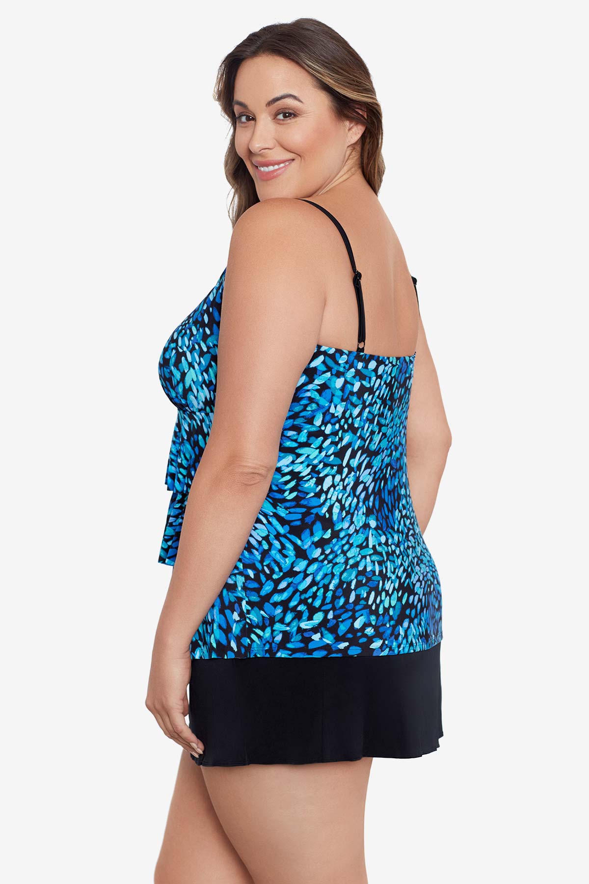 Woman turned left wearing a black and blue petal pattern ruffle faux skirtini one-piece swimsuit