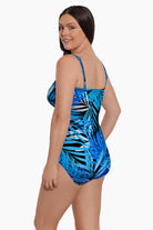 Woman turned left wearing a blue palm leaf printed bandeau with straps one-piece swimsuit