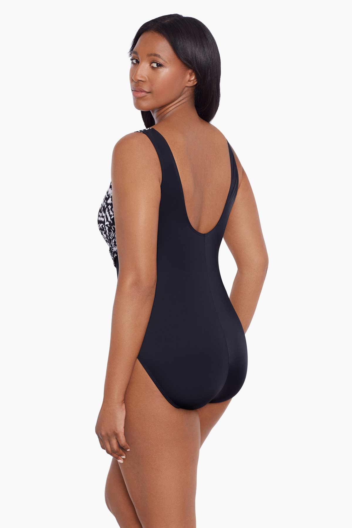 Woman turned left wearing a black and white abstract printed one-piece swimsuit with mesh cutout on the side