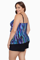 Woman faced left wearing a blue and green streak printed ruffle shortini swimsuit