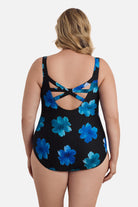 Woman faced away wearing a large blue flower printed one-piece swimsuit with an X back