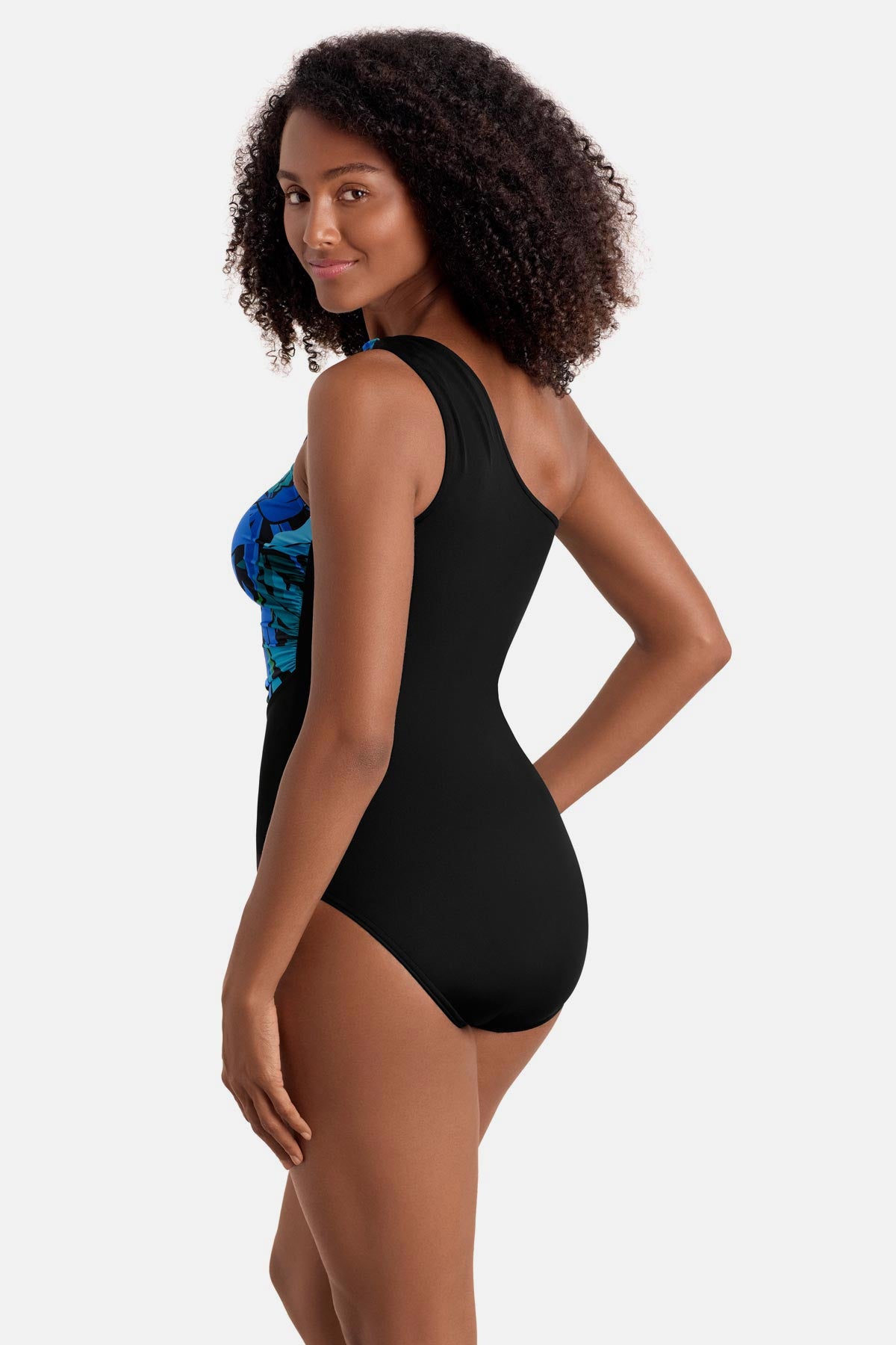 Woman turned left wearing a blue and green palm leaf printed one shoulder one-piece swimsuit