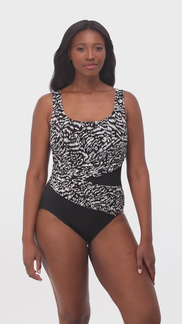 Woman wearing a black and white abstract printed one-piece swimsuit with mesh cutout on the side