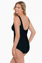 Woman turned left wearing a black one-piece swimsuit with black and white ruffles down the front