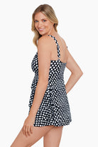 Woman turned left wearing a black and white polka dot tiered ruffle swim dress