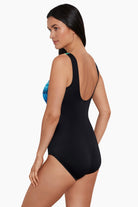 Woman turned left wearing a black and blue tie-dye-esque printed one-piece swimsuit