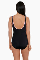Woman faced away wearing a black one-piece swimsuit with white piping on the straps