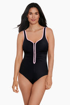 Woman wearing a black one-piece swimsuit with white piping down the front and on the straps