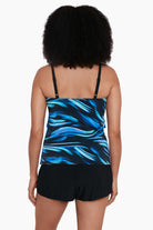 Woman turned away wearing a black and blue oil slick print ruffle tiered one-piece swimsuit shortini