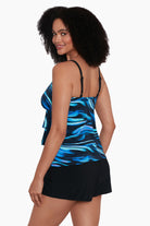 Woman turned left wearing a black and blue oil slick print ruffle tiered one-piece swimsuit shortini